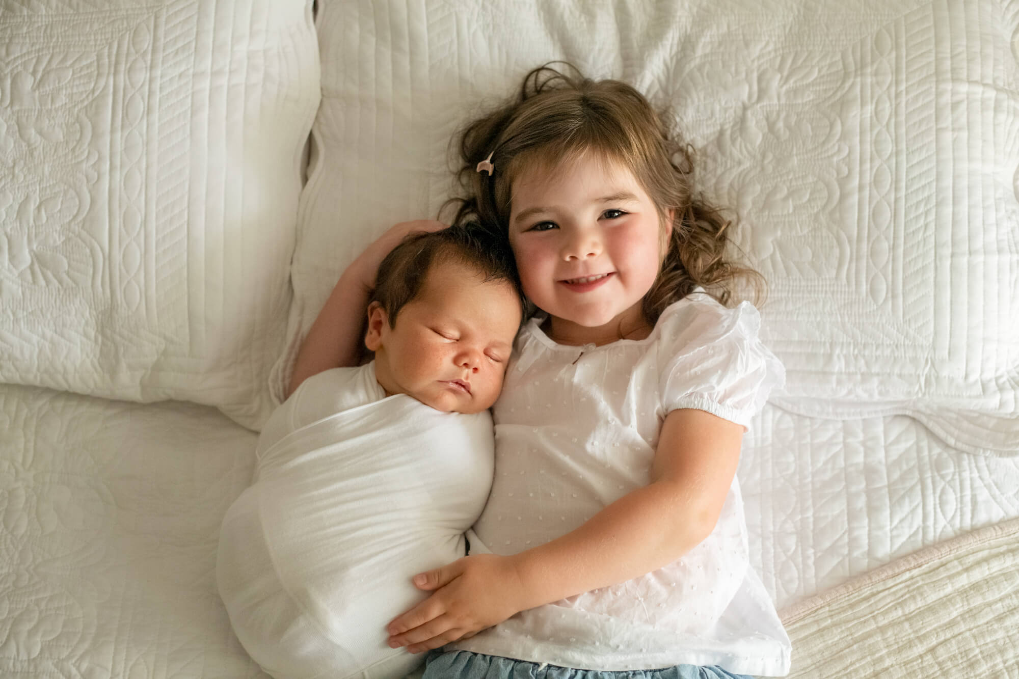 little girl hugging her newborn sibling on a bed Edmonton Baby Stores