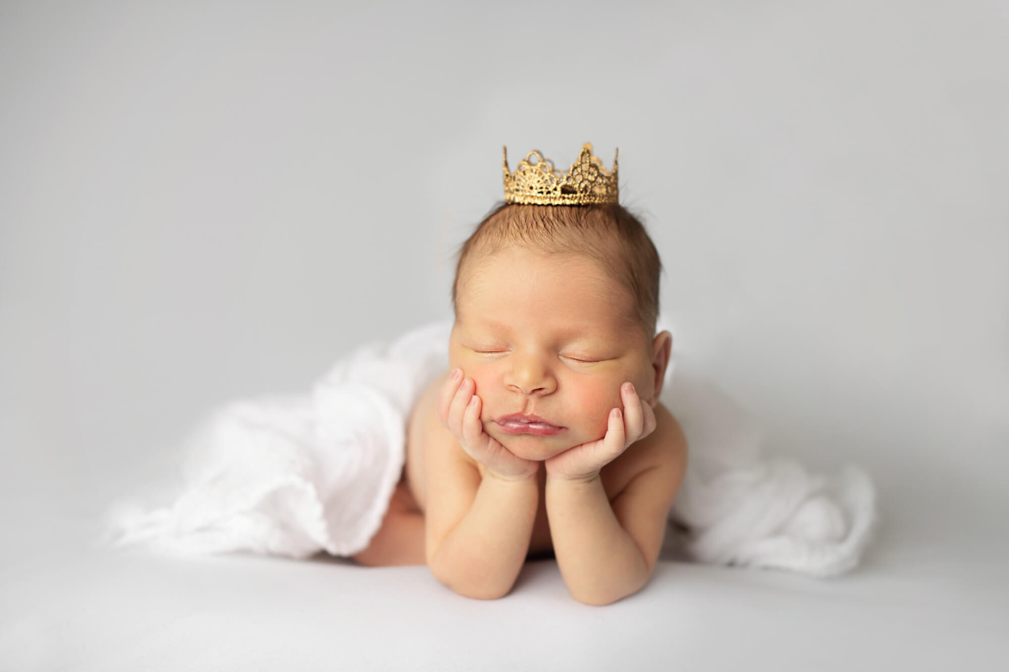 newborn baby wearing a crown and leaning on their hands