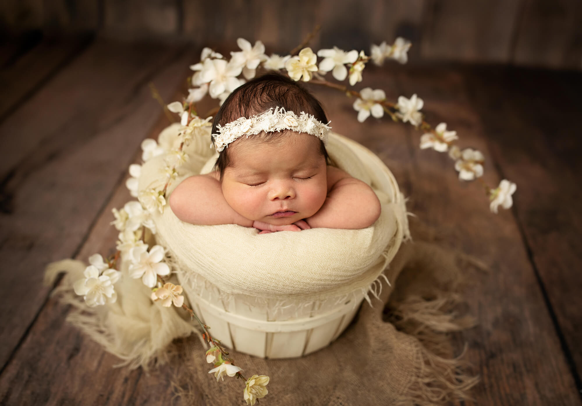 newborn baby girl in white headband with flowers on dark wood floor drop